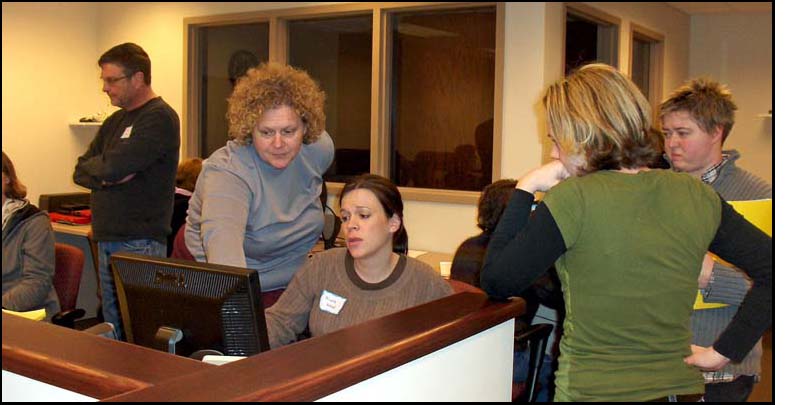 Photo shows the same 3 women at the computer, the one sitting down is looking concerned a fourth woman is pointing to something on her screen.