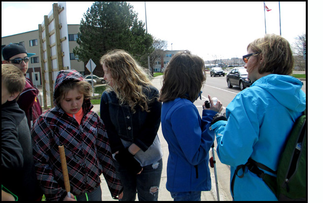 Photo shows several of the students standing on the sidewalk with instructor Denise talking with them.