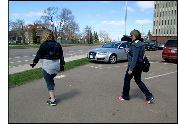 Photo shows a student walking across the parking lot, followed by instructor Josee holding a stopwatch.