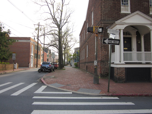 Residential: Four photos show an intersection of a 2-lane street and a 3-lane street with a two-story brick home with a small covered porch on one corner, a two-story wooden house on the other, and a large brick church on the third corner.  The streets are paved with concrete, and all 4 corners have red brick sidewalks whose curbramps have detectable warning made of two rows of one-foot-square white cement tiles each having 6 rows of 6 truncated domes.