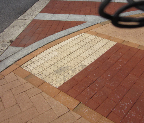 Garage entrance: Five photos show a brick driveway entering a parking garage, with salmon-colored brick sidewalks on each side of the driveway (about 15 feet from each side of the driveway, the sidewalk changes to red brick).  Each side of the driveway has a curbramp near the bottom of the driveway facing diagonally toward the street.  Each curbramp has a rectangle of red bricks outlined with orange brics -- the rectangle is about 4 feet wide at the bottom of the curbramp and extends into the sidewalk about 8 feet.  The bottom 2 feet of this rectangle is made with white concrete detectable warning (2 rows of one-foot-wide square tiles each with 6 rows of 6 truncated domes).