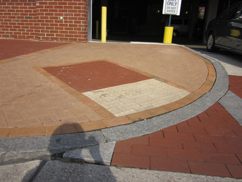 Garage entrance: Five photos show a brick driveway entering a parking garage, with salmon-colored brick sidewalks on each side of the driveway (about 15 feet from each side of the driveway, the sidewalk changes to red brick).  Each side of the driveway has a curbramp near the bottom of the driveway facing diagonally toward the street.  Each curbramp has a rectangle of red bricks outlined with orange brics -- the rectangle is about 4 feet wide at the bottom of the curbramp and extends into the sidewalk about 8 feet.  The bottom 2 feet of this rectangle is made with white concrete detectable warning (2 rows of one-foot-wide square tiles each with 6 rows of 6 truncated domes).