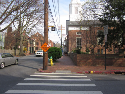Residential: Four photos show an intersection of a 2-lane street and a 3-lane street with a two-story brick home with a small covered porch on one corner, a two-story wooden house on the other, and a large brick church on the third corner.  The streets are paved with concrete, and all 4 corners have red brick sidewalks whose curbramps have detectable warning made of two rows of one-foot-square white cement tiles each having 6 rows of 6 truncated domes.