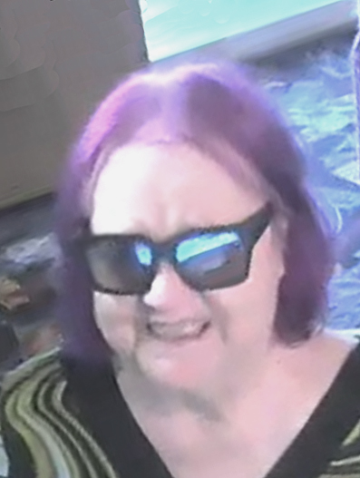 Ann Byington is a white woman with pink hair that is shoulder-length, wearing sunglasses and smiling broadly as she speaks.