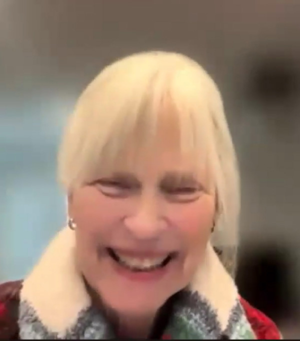 Marjie Wood is a white woman with light blond hair, wearing a plaid sweater and smiling broadly.