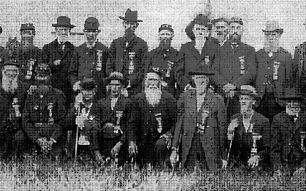 photo shows about 20 men standing or squatting in an open field.  They are all elderly, most with full beards, some are holding swords.