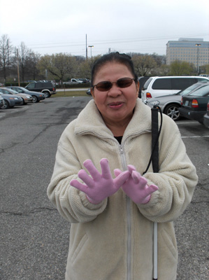 Nanta stands in the parking lot with both gloves on, with a big smile.  She wears a coat and is holding a long cane.