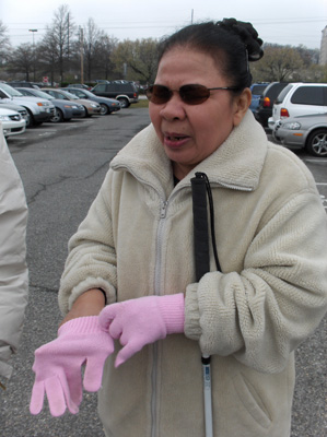 two pictures show Nanta in a parking lot with one glove on, and the other hand in a glove with the fingers going into random parts of the glove.  She looks like she is puzzled and concentrating