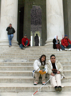 Photo shows Nanta and Ann sitting on marble steps leading up to the columns, the statue of Jefferson is visible behind the columns.  Three other people are sitting on other parts of the stairs and one person is leaning against a column.