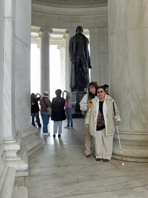 Photo shows the inside of the Jefferson Memorial, which has many columns surrounding a statue of Jefferson standing about 20-30 feet tall.  Ann and Nanta are standing in front of one of the columns.