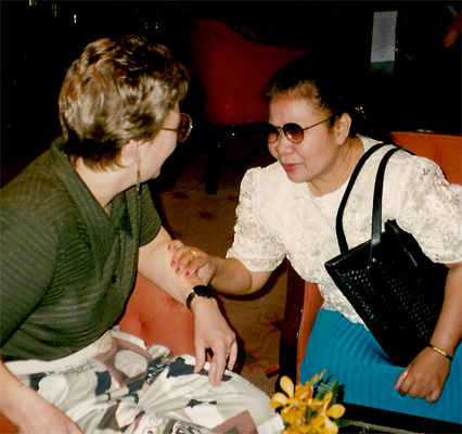 Nanta and Dona are facing each other in the lobby chairs.  Dona is smiling, and Nanta is leaning forward and smiling while reaching out to touch Dona's arm.