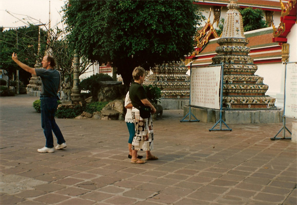 Nanta and Dona are walking on the patio of the temple, with some ornate buildings in front of them.  Behind them David is signaling to someone out of the picture. 