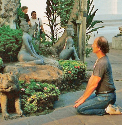 David sits on his knees in front of a small statue of a goddess serenely sitting on her knees.  In the background are the sillouettes of Dona and Nanta.