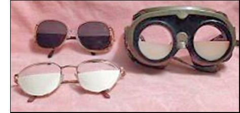 Photo shows sunglasses with tape inside the bottom half of the lens; goggles with cardboard semicircles screwed into the bottom half of each lens opening; glasses with paper semicircles taped outside the bottom half of each lens