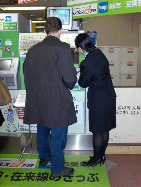 photo shows a customer (Stephan Sauerburger) standing in front of a ticket machine;  next to him is a woman wearing a uniform, pointing out something on the machine.