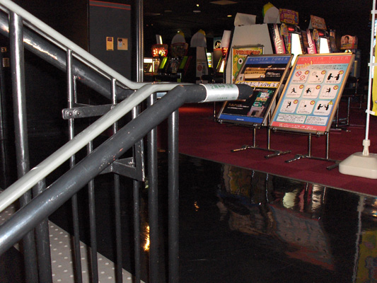 3 photos show a stairway with a round metal railing, which has a braille metal label wrapped around the ends at the bottom and top of the stairs.  On the floor, along the top of the stairs, is a strip of detectable warning surface about a foot wide.