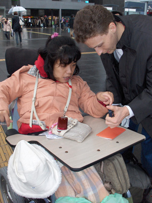 3 photos show Stephan and a young Japanese woman in electric wheelchair with tray.  Stephan is holding her address book and she is pointing to it.