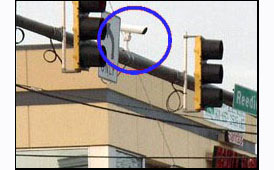 Photo shows a camera shaped like a tube, attached to the bar that holds the traffic signals.