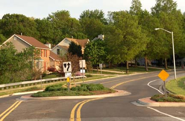 photo shows a residential street 3 lanes wide, a cirle with plants fills the middle lane, and just before the cirlce from each direction the curb and grass extend in the street (a 'bulbout') for about half a lane, so that approaching vehicles must swerve to the left to miss the bulbout and then must swerve to the right to get around the circle