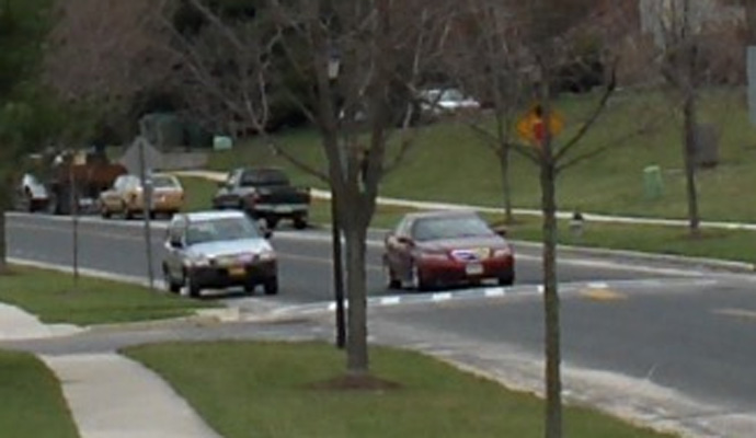 photo shows close-up of the speed hump, which extends across the street.  A car approaches it and starts to ride over the hump.