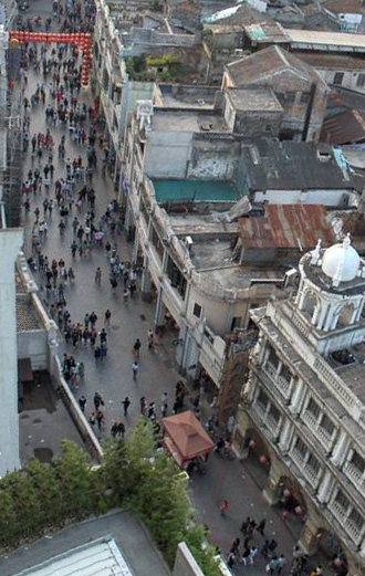 photo looks down from about 15 stories onto a narrow, gently turning street with no vehicles, many people walking in the street but about half as crowded as the night photos.
