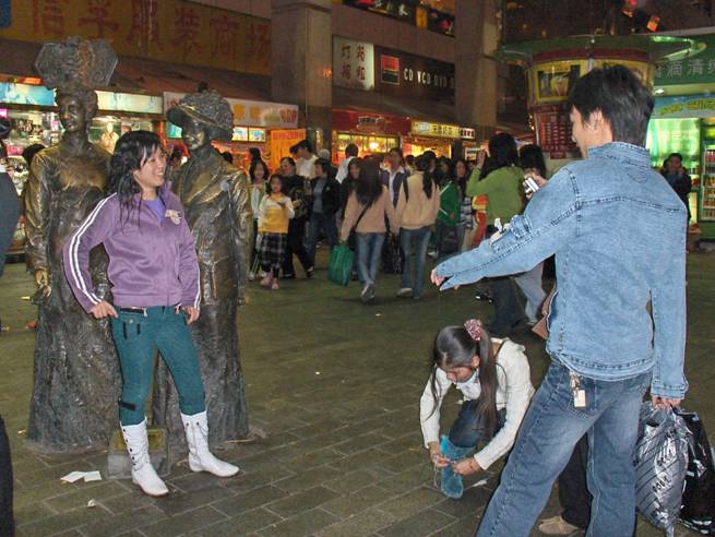 photo shows life-sized statues standing in the plaza, with a woman posing between them.