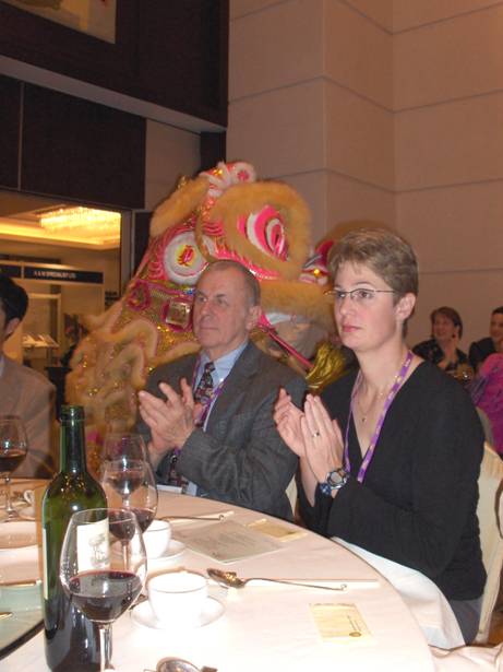 photo shows two people sitting at a table and applauding unaware that behind them is a Chinese dragon approaching the stage.