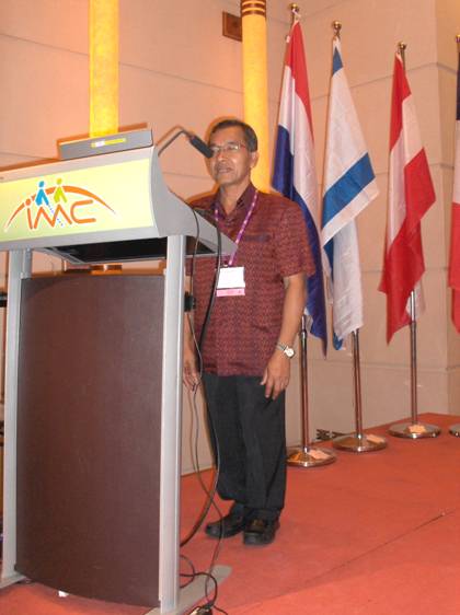 Chalam Yam-Iam is standing behind the podium -- behind him are a row of flags.