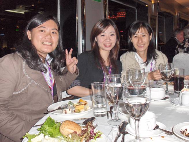 3 women sit at the dinner table and smile, one holds up two fingers in a 'V'