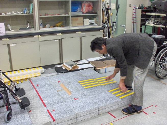Photo shows Professor Nakamura placing two mats with raised yellow lines on a platform that is about 6 inches high.