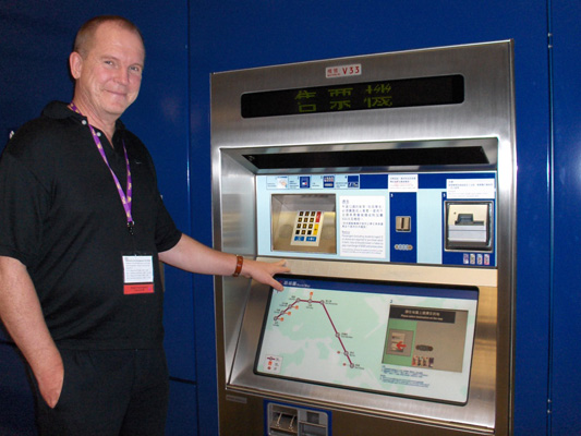Bengt has his hand on the display on the wall, with a map of the train routes at the bottom, and a keypad and slots at the top.