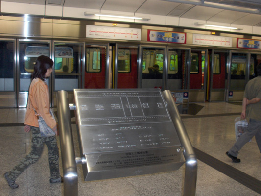 2 photos show map on a stand on the platform, with a tactile strip leading to the front of the map.  The edge of the platform has a glass wall with doors that open when the train arrives (the train has arrived in the second photo).