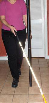 series of photos shows a woman walking toward a pole with a cane in her right hand.  the cane tip starts on the woman's left, misses the pole as it moves to the woman's right, and when it reaches left again the entire cane is beyond the pole and the woman bumps into the pole with her left shoulder.