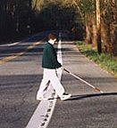 photo shows the boy reaching the other side of the street -- his cane has crossed the white line at the edge of the street's shoulder.