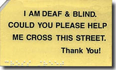 Photo shows a yellow laminated card with braille along the bottom and the left upper corner cut off.  The 1st line says 'I AM DEAF & BLIND.' 2nd line says 'COULD YOU PLEASE HELP' 3rd line says 'ME CROSS THIS STREET.' 4th line says 'Thank you!'