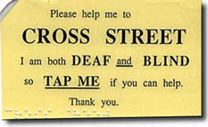 Photo shows a yellow card of the same shape and color with braille.  1st  line says 'Please help me to'  2nd  line in very large print says 'CROSS STREET' 3rd line says 'I am both DEAF and BLIND' 4th line says 'so TAP ME if you can help.' Last line says 'Thank you.'