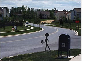 A stick figure/person on the corner faces a two-lane street.  To the right of the figure (east) the street is straight and goes slightly downhill for about 50 feet and then curves to the left and is visible going straight uphill for another half block.