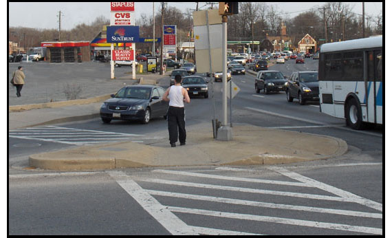 3 photos show a triangular island separating one lane for right-turning traffic from the remainder of the intersection.  The lane has a painted crosswalk from the island to the curb and in each picture, a pedestrian is waiting on the island or starting to cross the lane from the island to the curb.  On the island is a pole with a walk signal for the pedestrians crossing the streets on the other sides of the island -- there is no walk signal for pedestrians crossing the channelized lane.