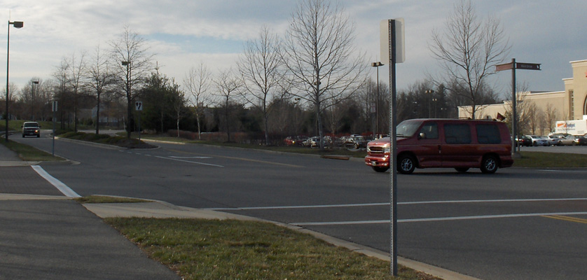 Photo shows a van starting to cross a 3-lane street from a stop sign.  To the van's right is a car approaching from about 40 feet away.