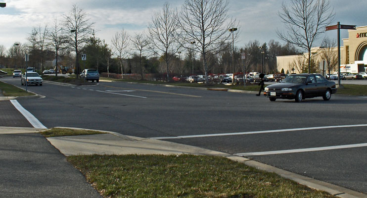 Photo shows a car starting to cross a 3-lane street from a stop sign.  A stick figure beside the car is also just starting to cross, and approaching the intersection to the figure's right is a car about 10 feet from the intersection.