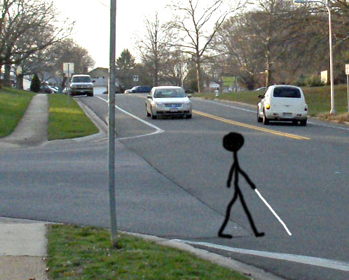 Photo shows the same intersection, with a car that is almost finished turning left from the side street into the main street while a car that had been approaching from the car's left is about 10 feet from the intersection.  A stick figure with a white cane is drawn just starting to cross the street.