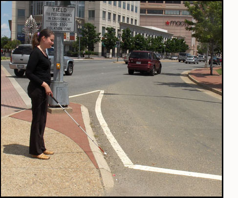 Two photos show Mimi holding a cane, standing on an island with streets diagonally to her left and right, and facing a lane for right-turning traffic.