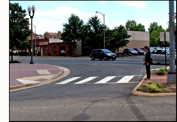 Two photos show Mimi holding a cane, standing on an island with streets diagonally to her left and right, and facing a lane for right-turning traffic.