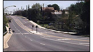 Photo shows a stick figure at a crosswalk on a 4-lane street with no stop signs or signals or intersecting streets for about a block in both directions.