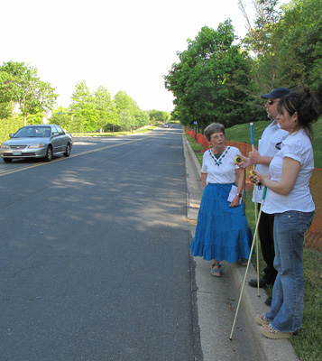 6 photos show Paul and Jomania standing at the side of a straight street with no parked cars. Dona is talking with them and pointing out cars coming from their right or left.
