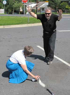 Photo shows Dona spray-painting a line in the parking lot while Fred screams out and has his arms raised to stop her.