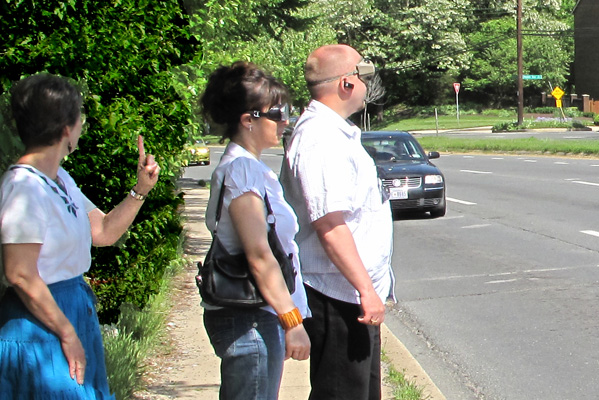 2 photos show two students wearing occluders at the edge of a two-way street with 4 lanes coming from the left, 3 lanes from the right.  Each photo has a car in one of the lanes from the left. Dona is behind the students and holding up fingers indicating whether the car is in the first, second, or third lane.
