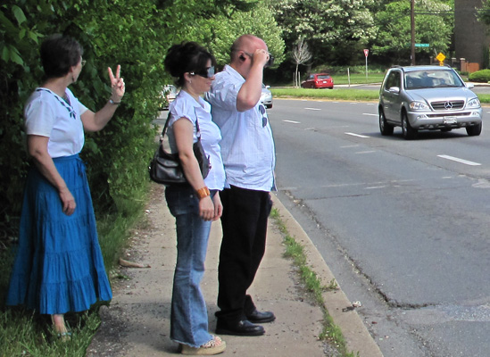 2 photos show two people wearing occluders at the edge of a street with 4 lanes coming from the left, each photo with a car in one of those lanes. Dona is behind them and holding up fingers indicating whether the car is in the first, second, or third lane.