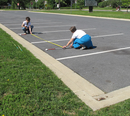 Photo shows Dona and Jomania with a tape measure, laying a second cane near the far side of the third parking space.