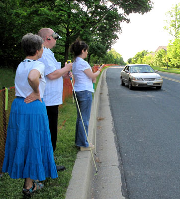 Photo shows Paul and Jomania looking to the left at a car approaching about 20-30 feet to their left.  Dona is standing to their right.